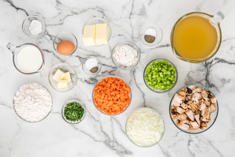 Chicken, chopped veggies, butter, flour, seasonings in glass bowls on white countertop