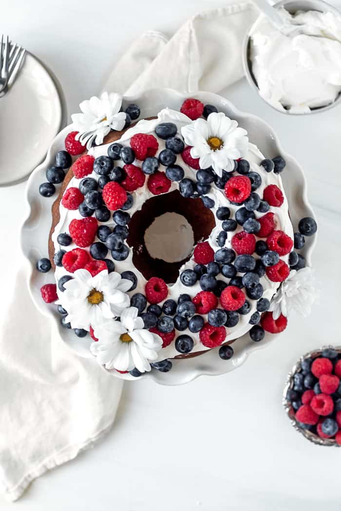Overhead shot of a butter pound cake recipe with whipped cream, raspberries and blueberries and edible flowers against white background ready to serve