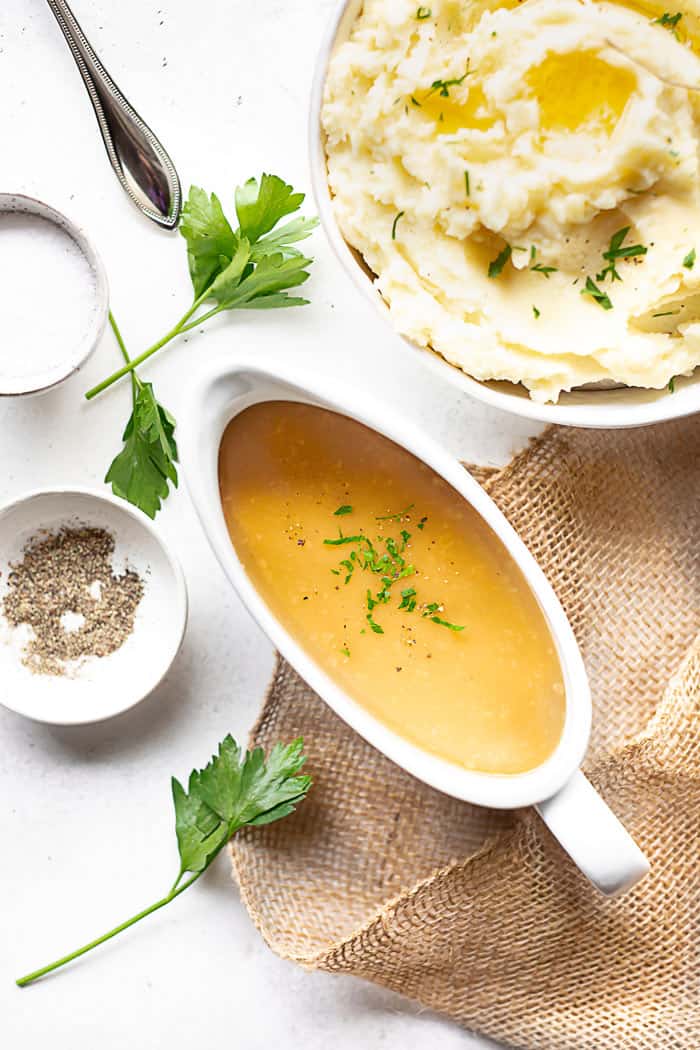 Homemade Gravy recipe in gravy boat with mashed potatoes and seasonings against white background