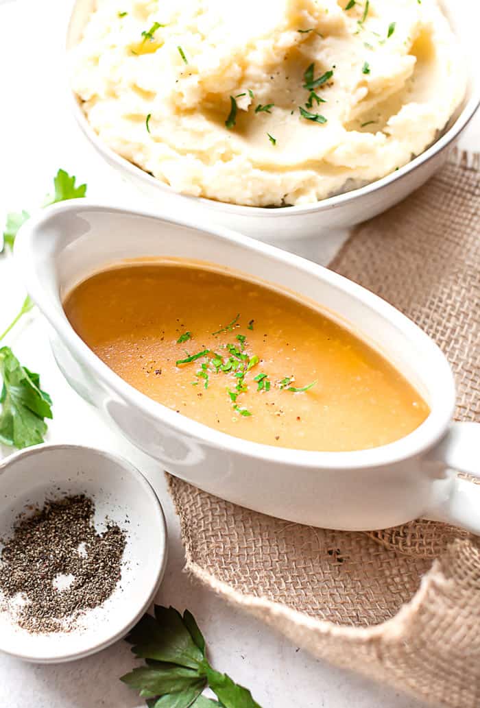 Homemade Brown Gravy from scratch in large white gravy boat with mashed potatoes and seasonings surrounding it