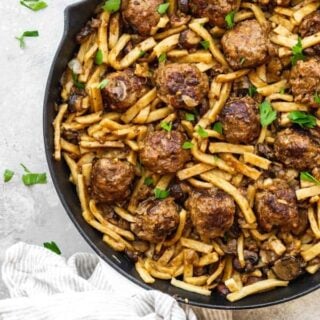 A large skillet of salisbury steak meatballs and noodles in a large skillet over white background with parsley sprinkle