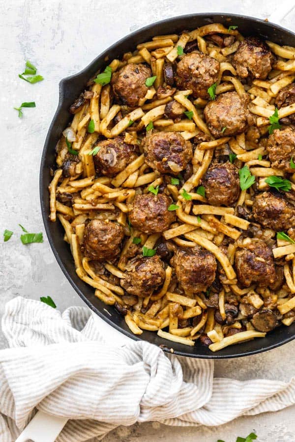 A large skillet of salisbury steak meatballs and noodles in a large skillet over white background with parsley sprinkle