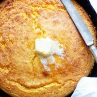 A close up of a Southern cornbread recipe with melting butter sliding down and a knife to cut slices