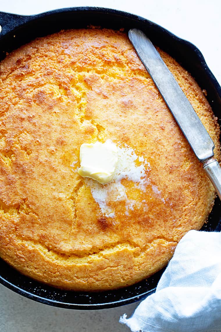 A close up of a Southern cornbread recipe with melting butter sliding down and a knife to cut slices