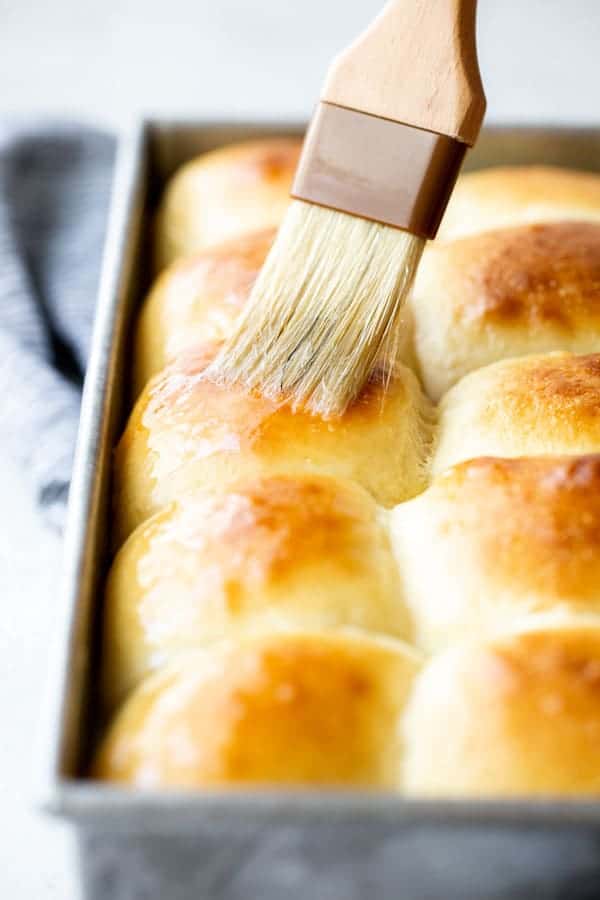 A close up of sweet rolls being brushed with melted butter