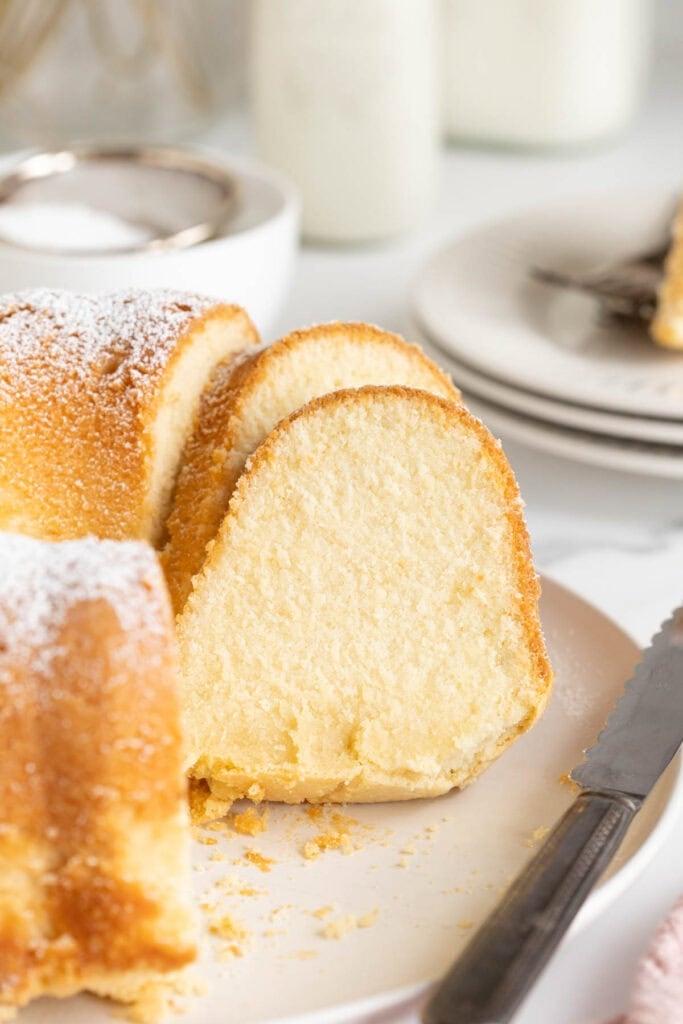 Slices of butter pound cake against a full cake on white plate with a knife