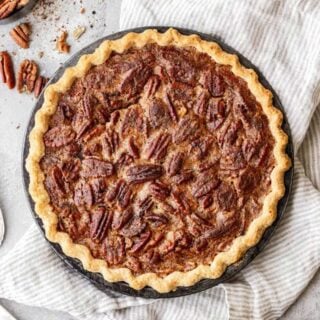 A whole Southern Pecan Pie in homemade butter crust with a bowl of pecans nearby against white background