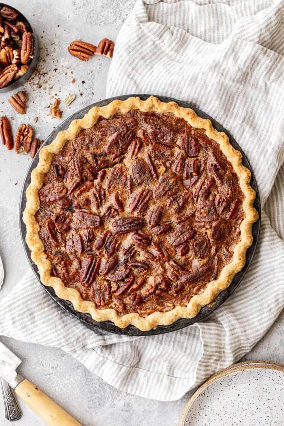 A whole Southern Pecan Pie in homemade butter crust with a bowl of pecans nearby against white background