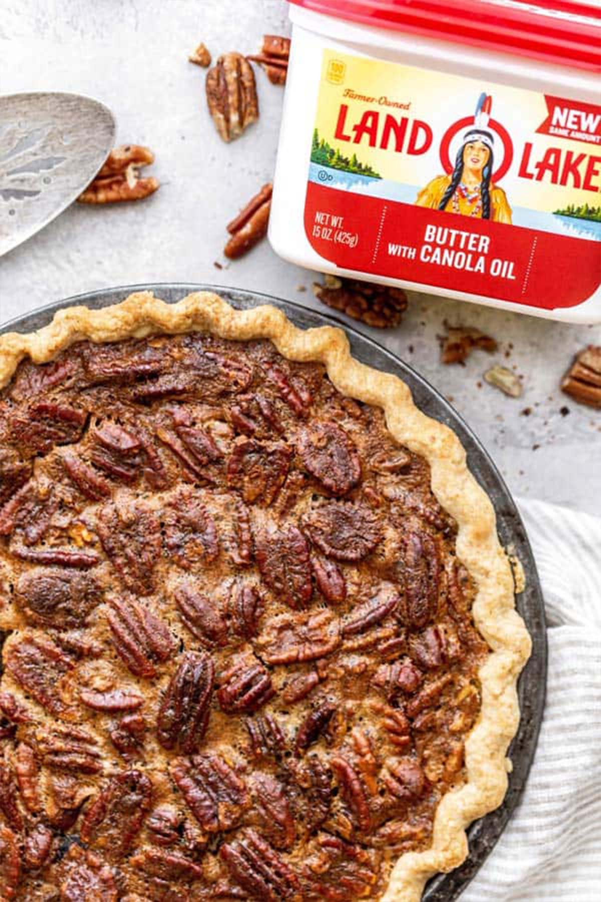 A large pecan pie against white background with pie server and butter package