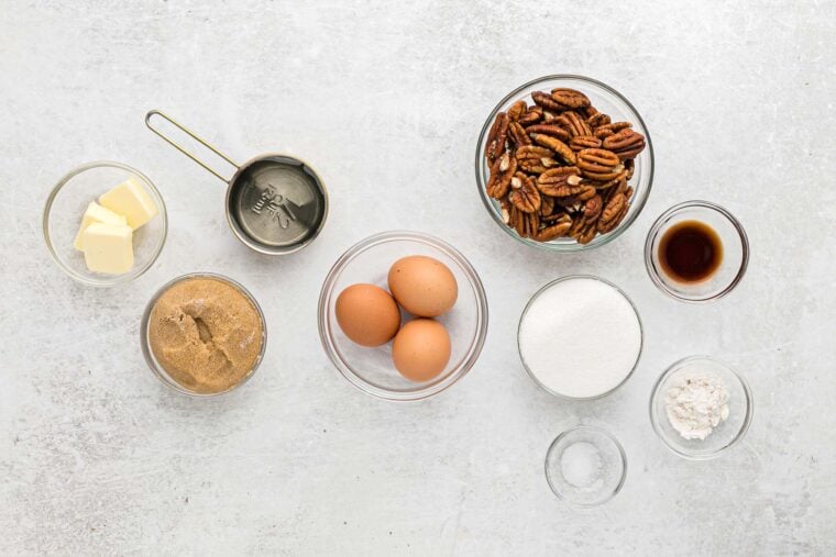 Ingredients to make best ever pecan pie on the counter ready to mix up in glass bowls on white countertop