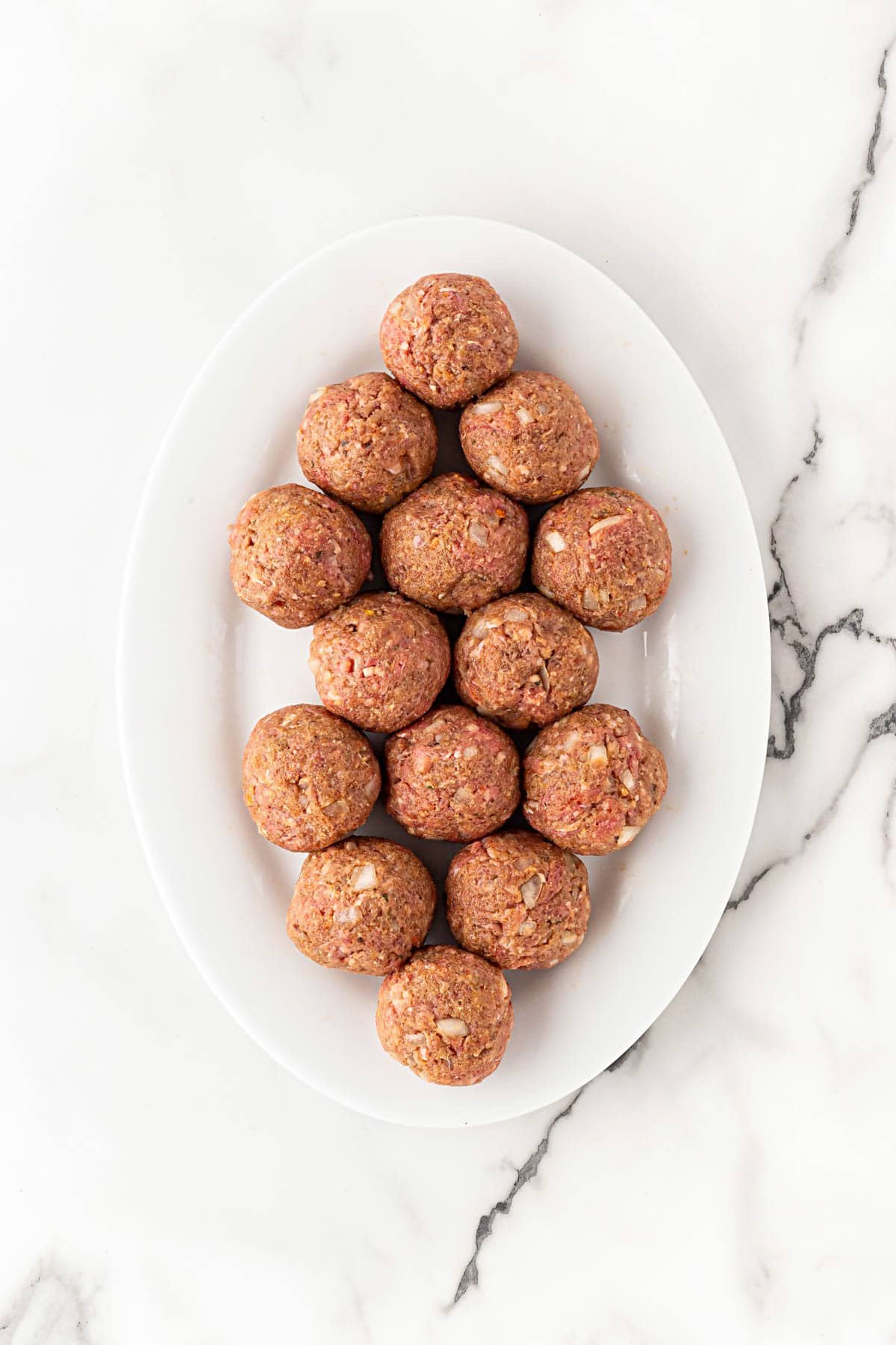 Raw Salisbury steak meatballs arranged on a white oval platter before cooking
