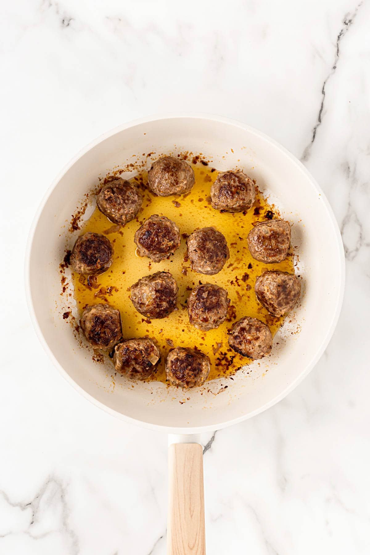 Salisbury steak meatballs browning in a skillet with melted butter and pan drippings