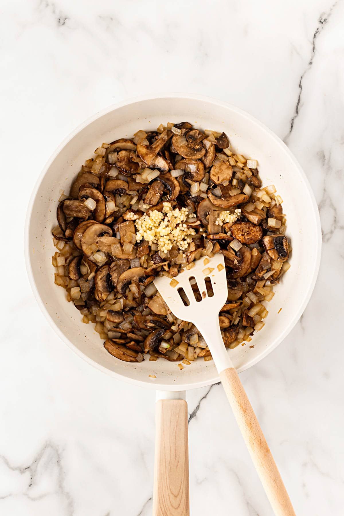 Sautéed mushrooms and onions cooking in a skillet with garlic added on top