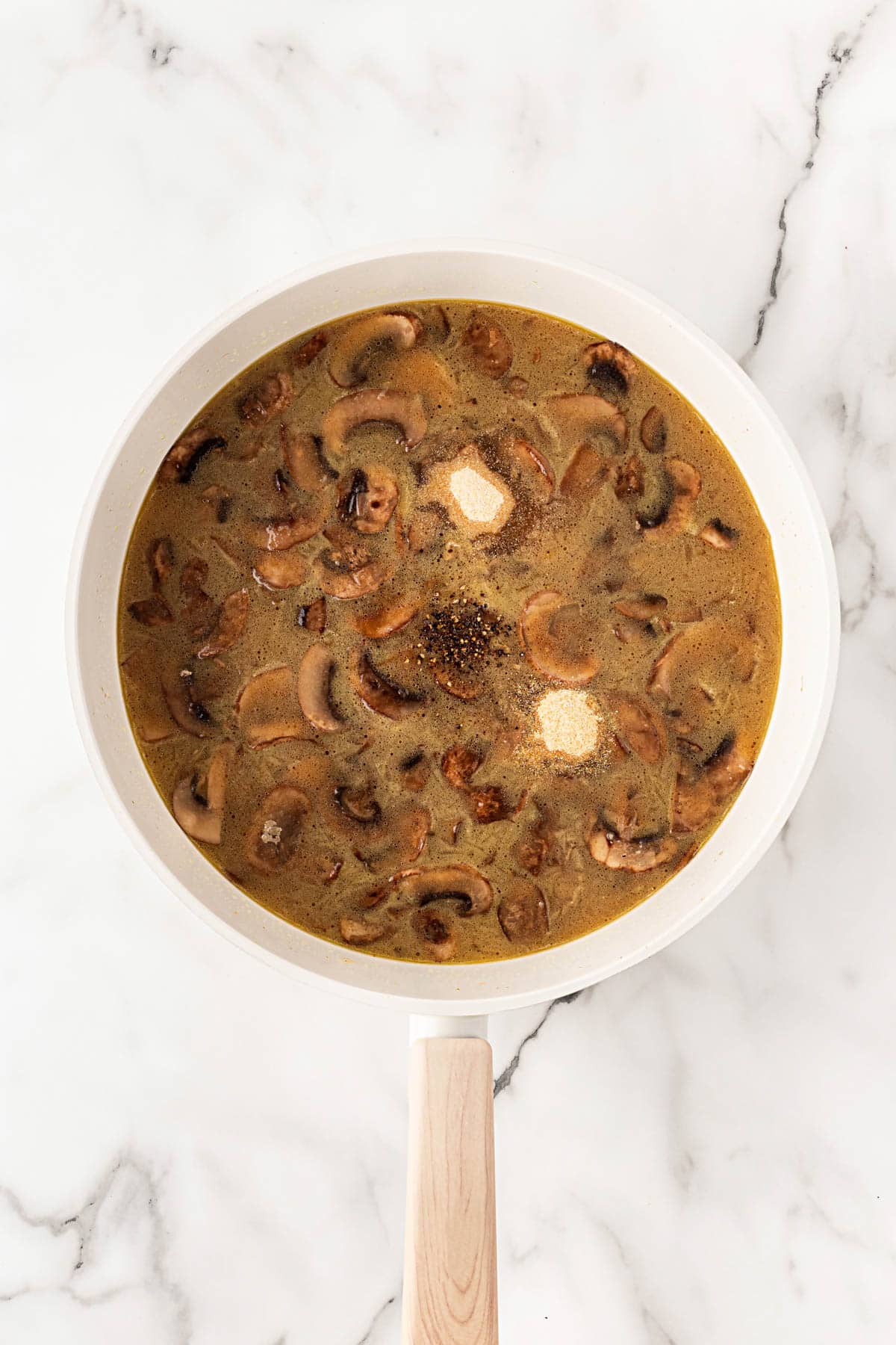 Beef broth poured into mushroom gravy base as it begins to thicken