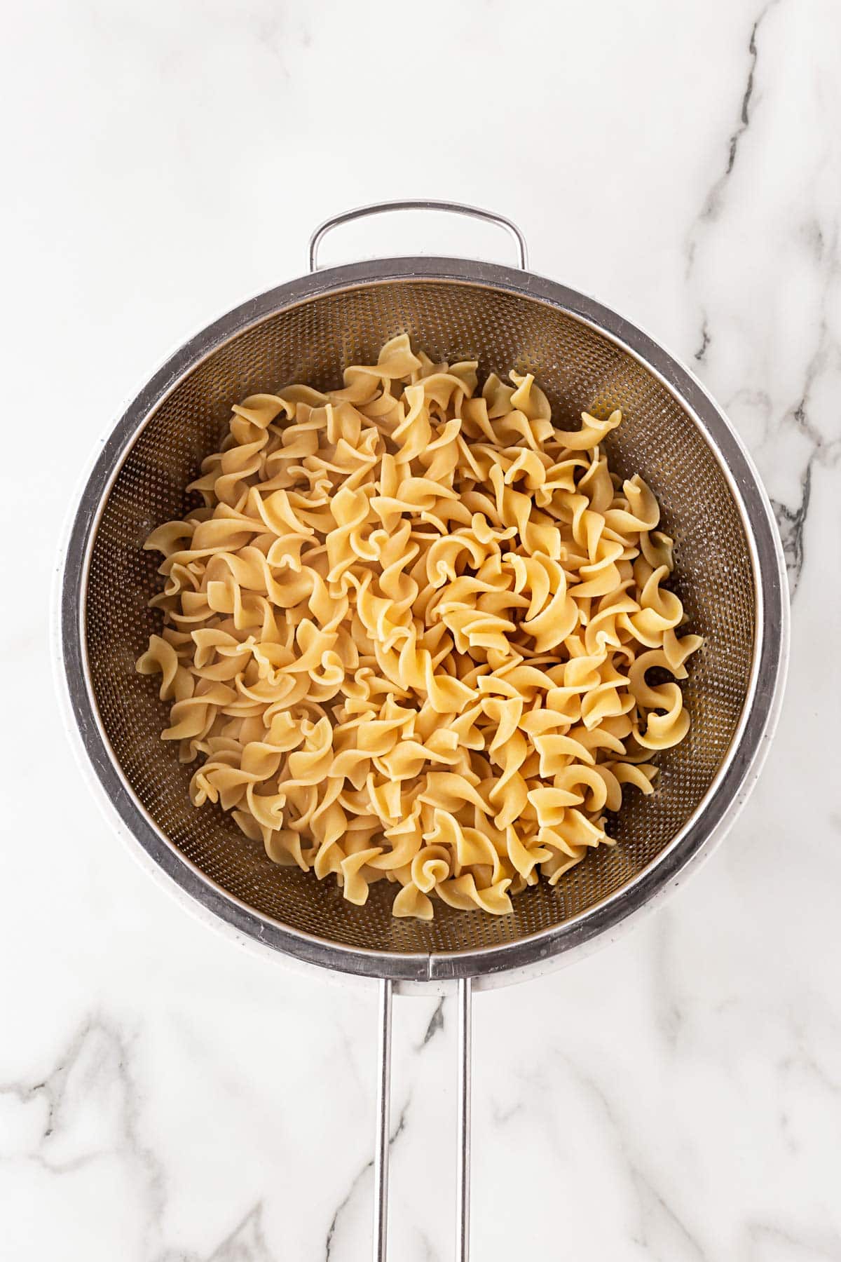 Cooked egg noodles draining in a metal colander