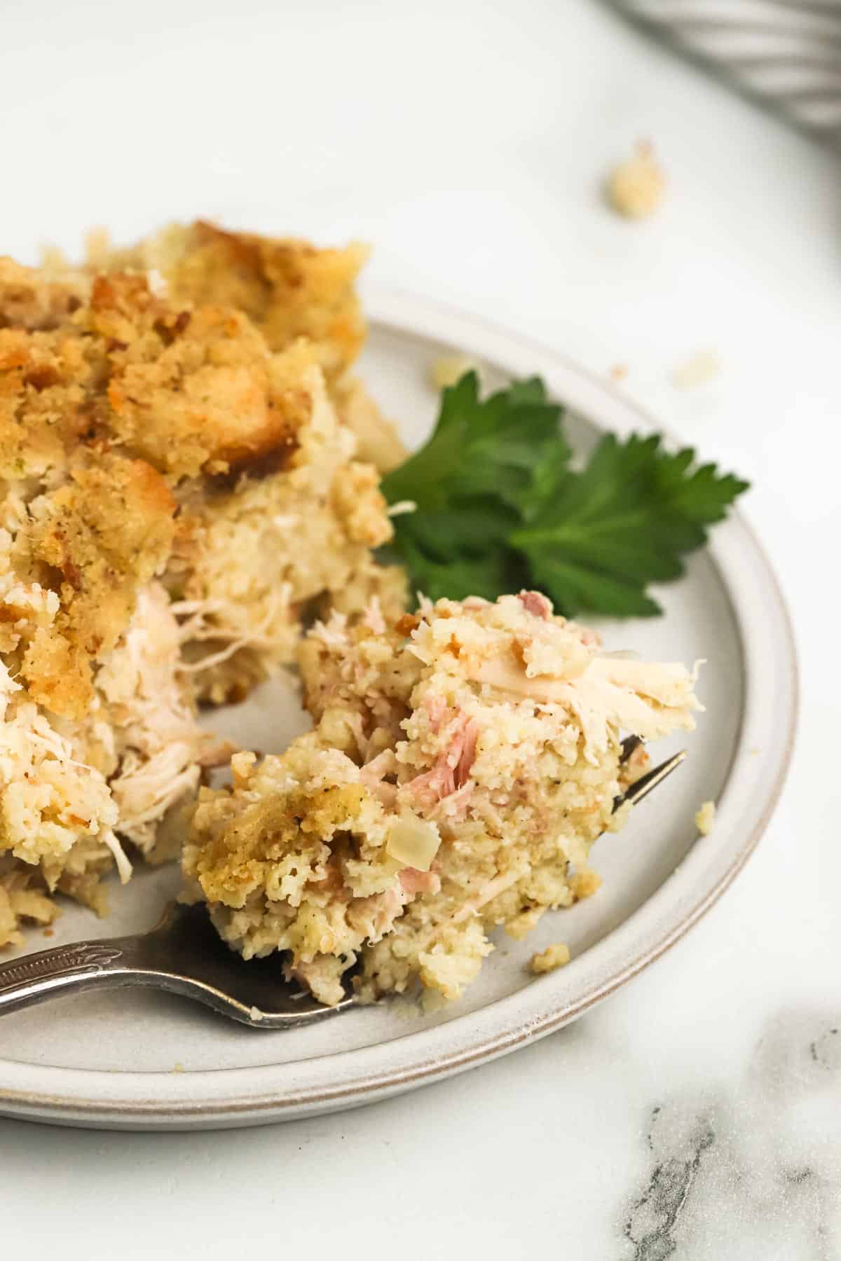 A plate with a serving of cornbread dressing with a fork on the plate with a bite on it.