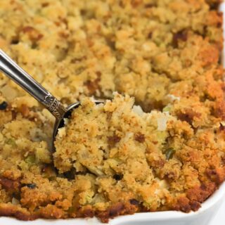 Casserole dish of southern cornbread dressing with a spoon scooping a serving up.