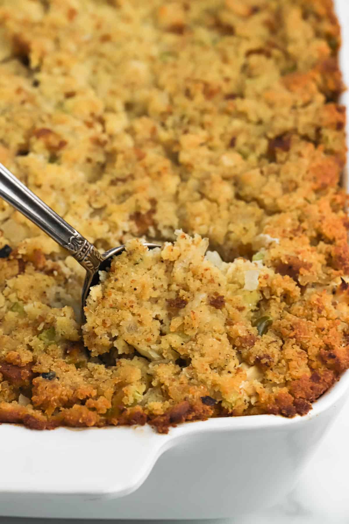 Casserole dish of southern cornbread dressing with a spoon scooping a serving up.