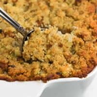 A spoon dipping into cornbread dressing in a white casserole dish.