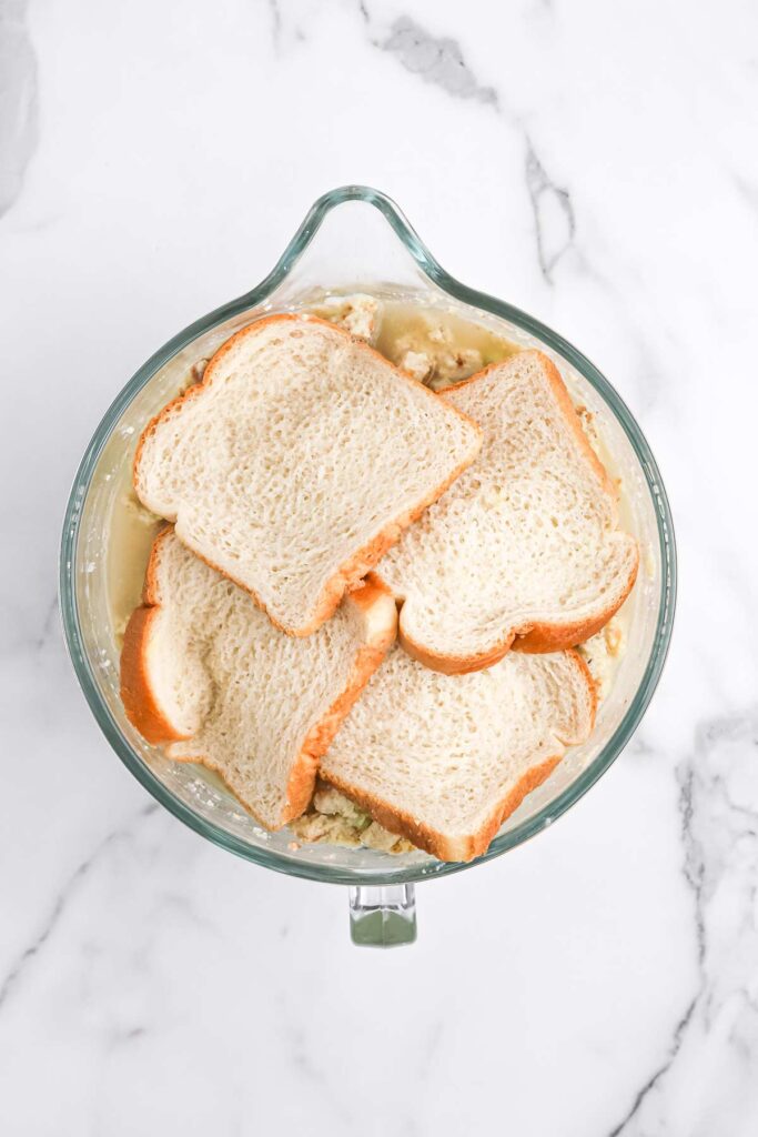Slices of bread added to the dressing mixture on white countertop.
