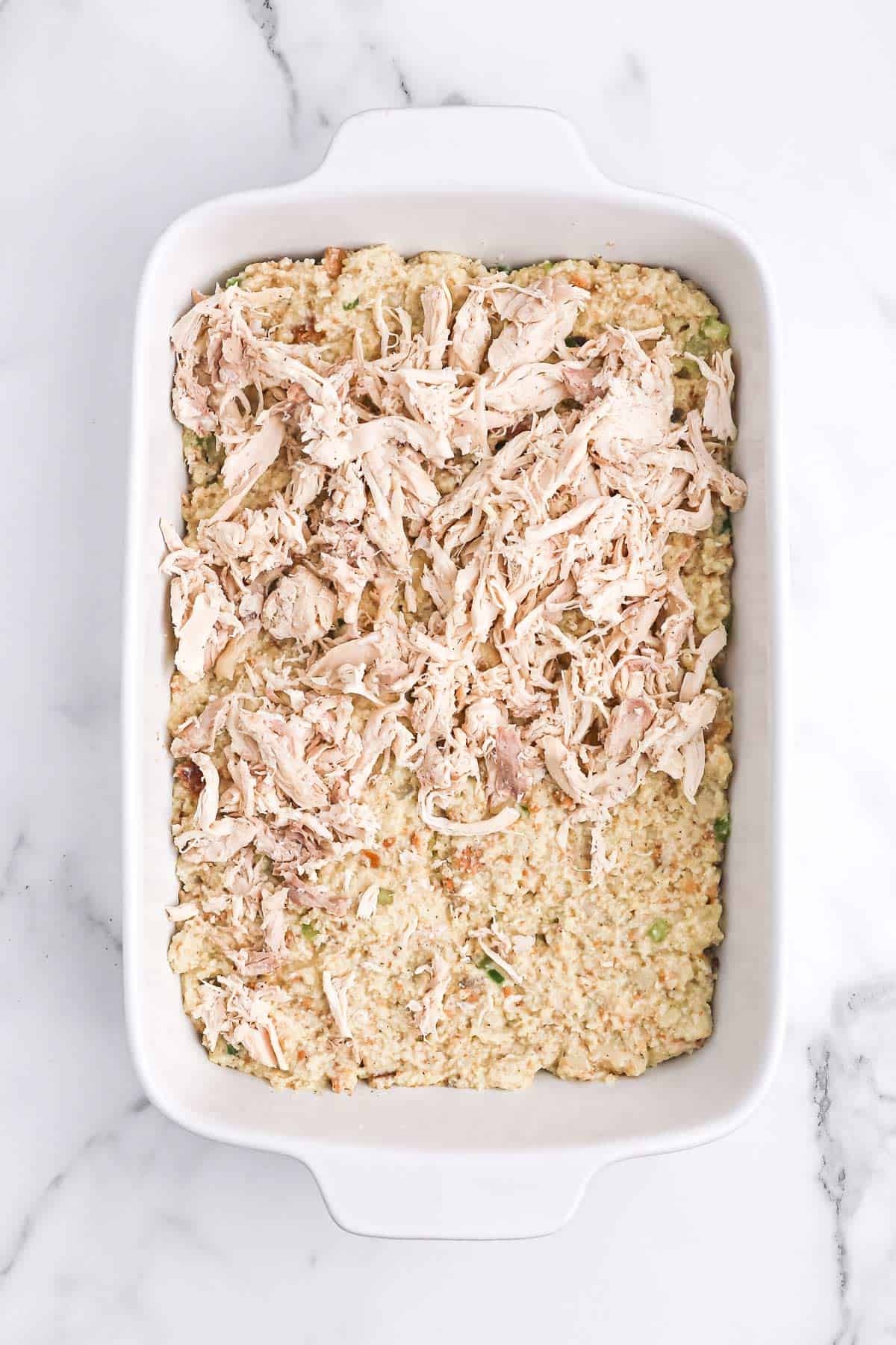 Dressing in a casserole dish topped with shredded chicken.