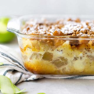 A powdered sugar sprinkled Apple Crisp French Toast Casserole ready to dig in with apples in background