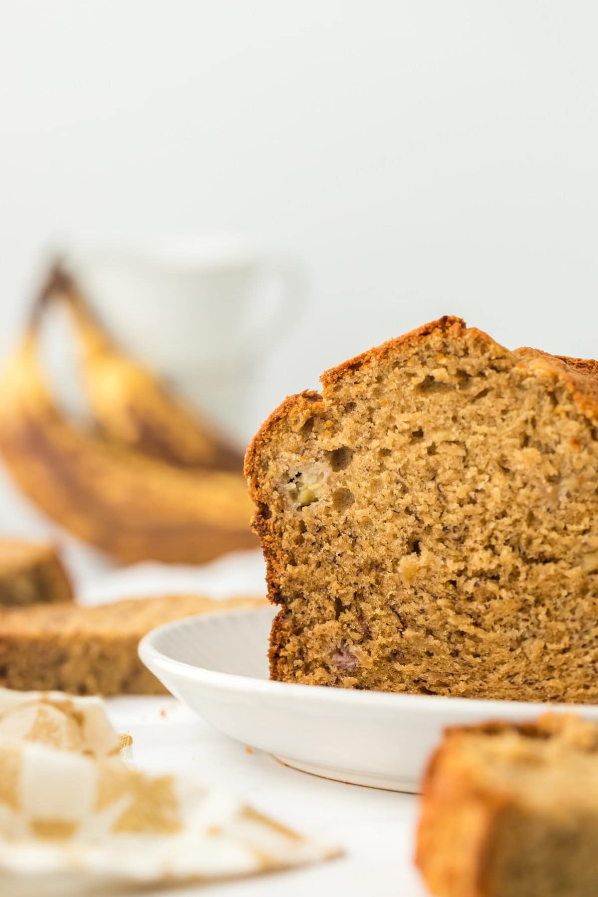 The best banana bread loaf cut open with ripe bananas in the white background and a white and yellow napkin nearby