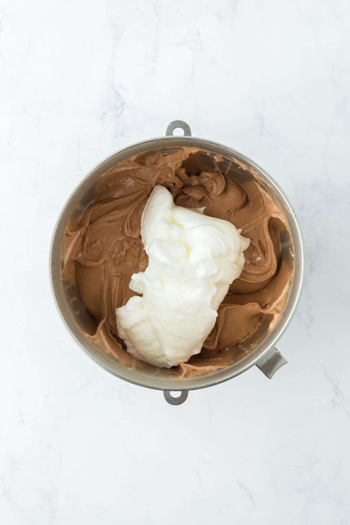 Egg whites in chocolate batter on white countertop.