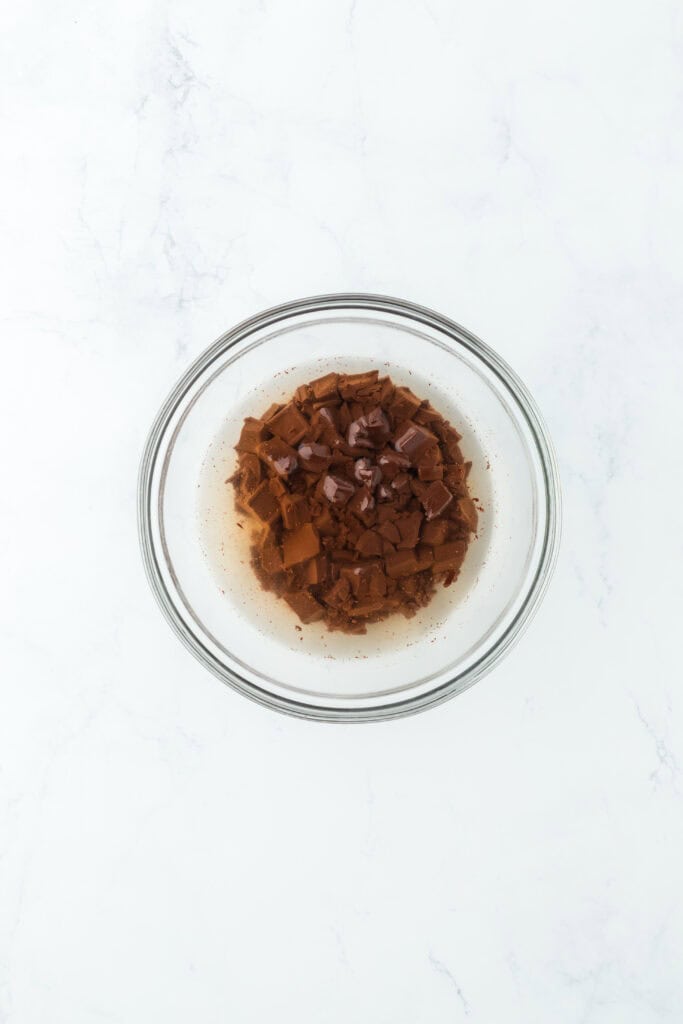 Chopped chocolate and boiling water in glass bowl.