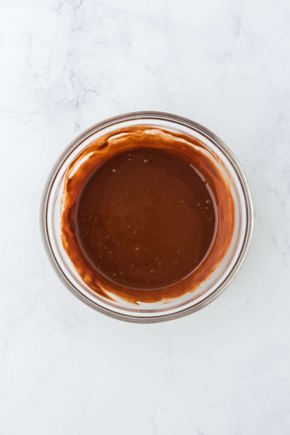 Smooth ganache in a glass bowl on a white countertop.