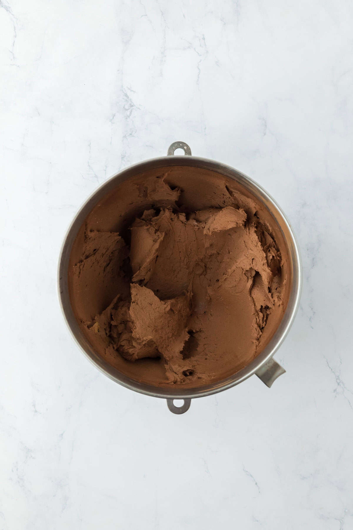 Chocolate frosting in a stand mixer bowl after being mixed until smooth.