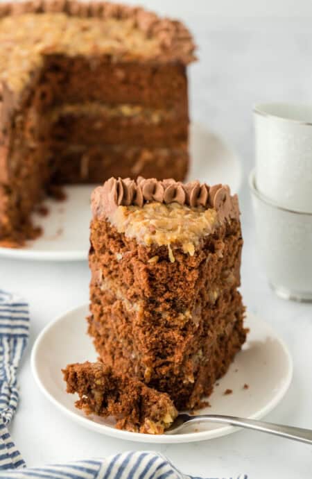 A slice of the best German chocolate cake recipe on a white plate being eaten with a fork