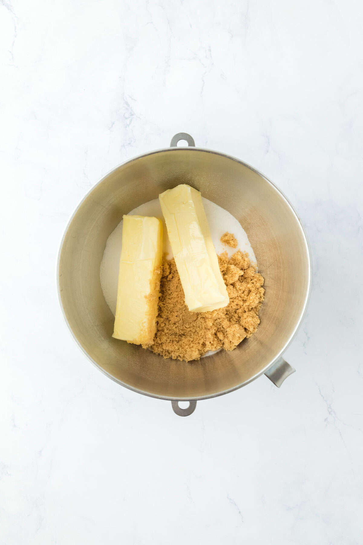 Butter and sugars in a mixer bowl on white countertop