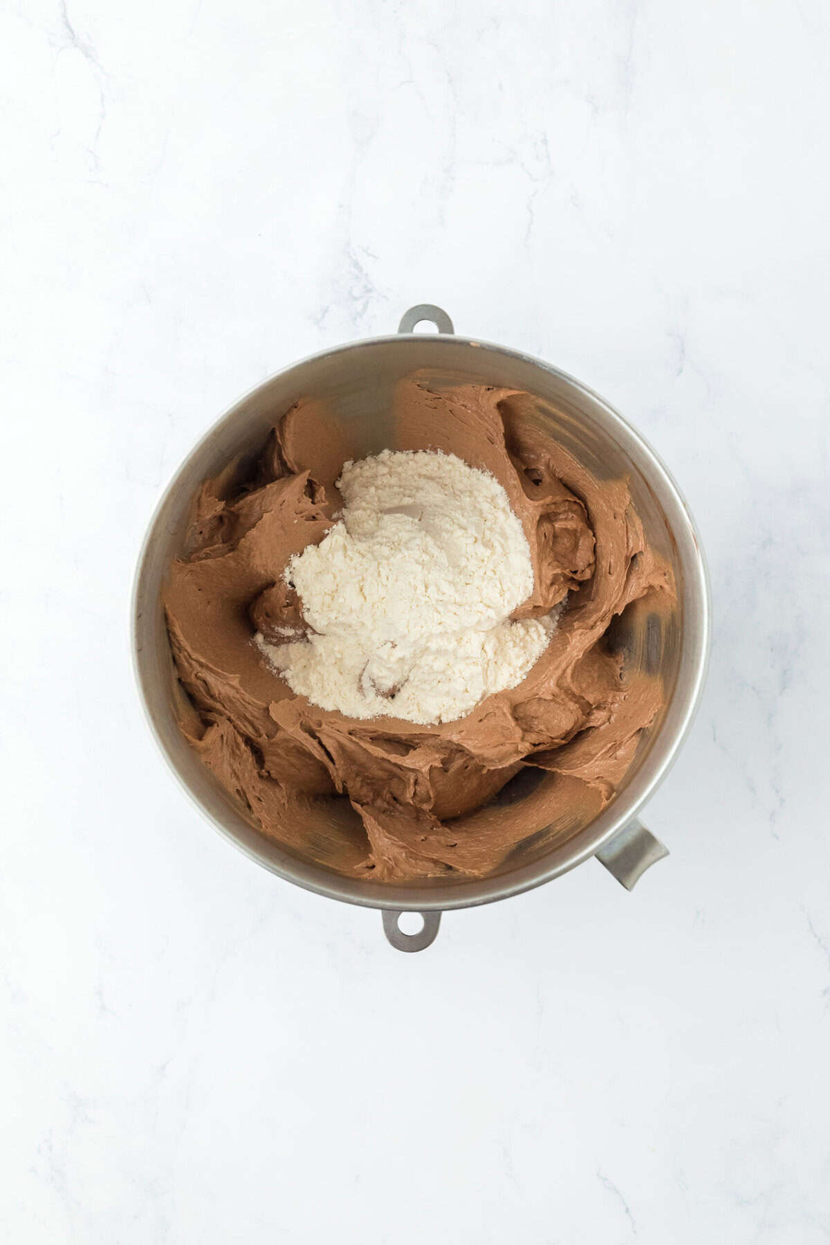 Flour mixture added to chocolate cake batter in mixer on white countertop.