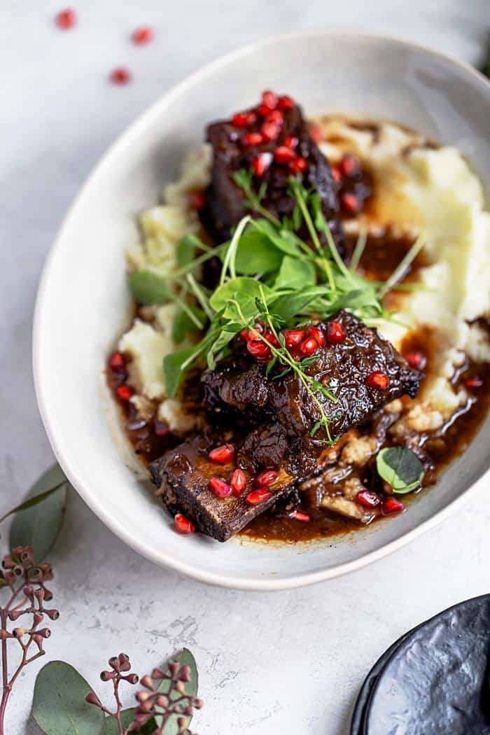 Pomegranate braised short ribs recipe served over mashed potatoes in a large white bowl