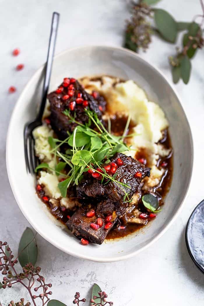 Close up of best braised short ribs over mashed potatoes in a white bowl with a fork ready to serve for the holidays
