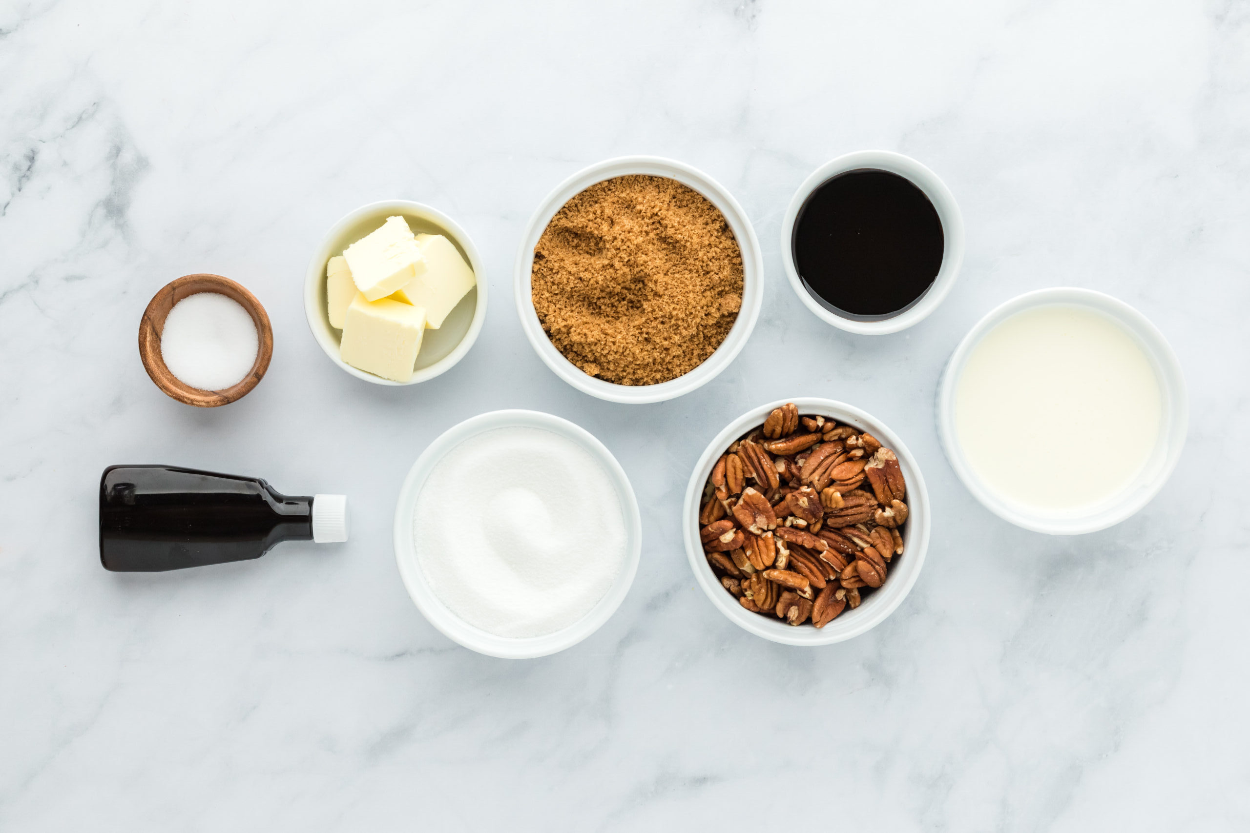 Brown sugar and white sugar, pecans, butter, vanilla in white bowls on white background to make praline recipe