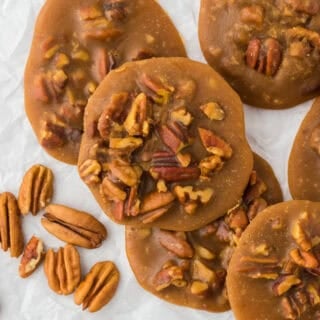 Pralines overlapping with pecans in the background on a white background