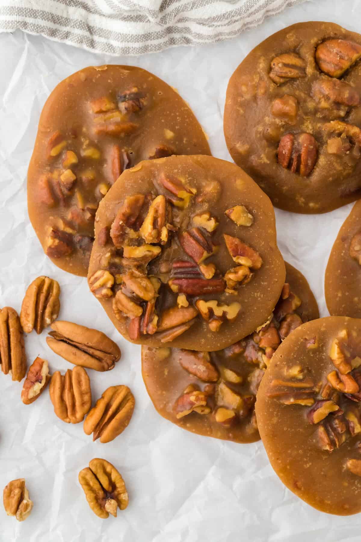 Pralines overlapping with pecans in the background on a white background