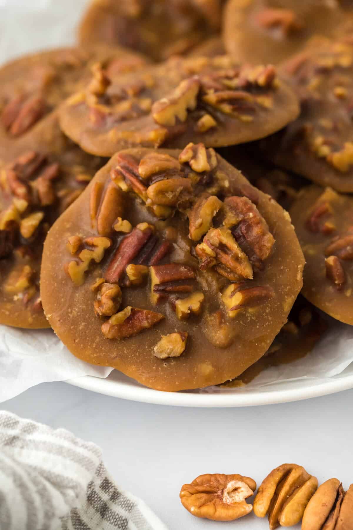 Pecan pralines stacked on a white plate in a white backgrouond