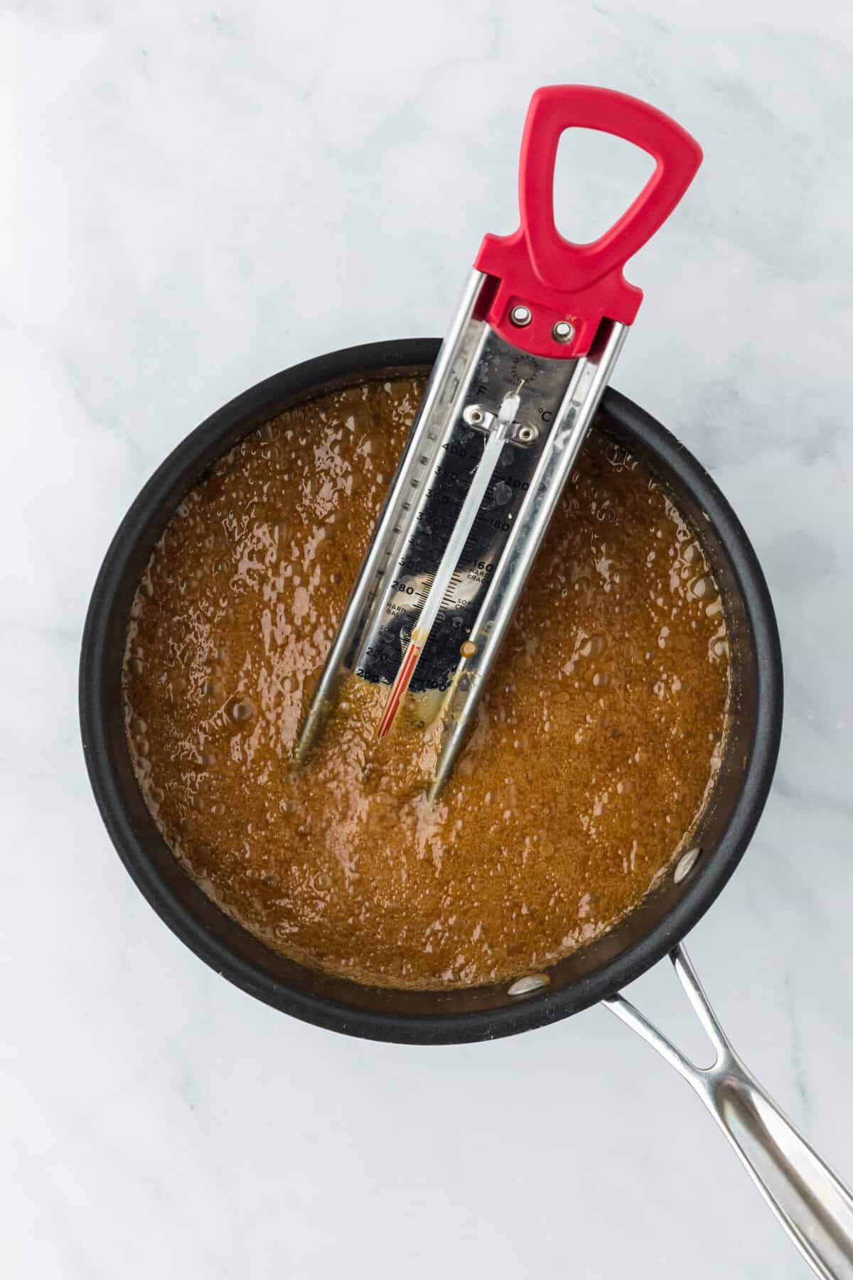 Praline syrup boiling in pot with candy thermometer on white background