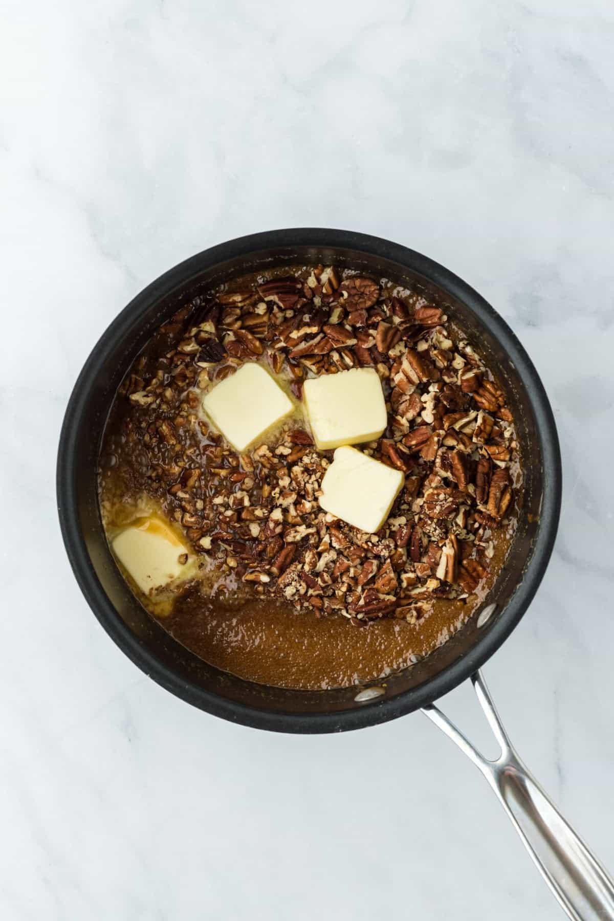 Butter, pecans, salt and vanilla added to praline mixture in pot on white background