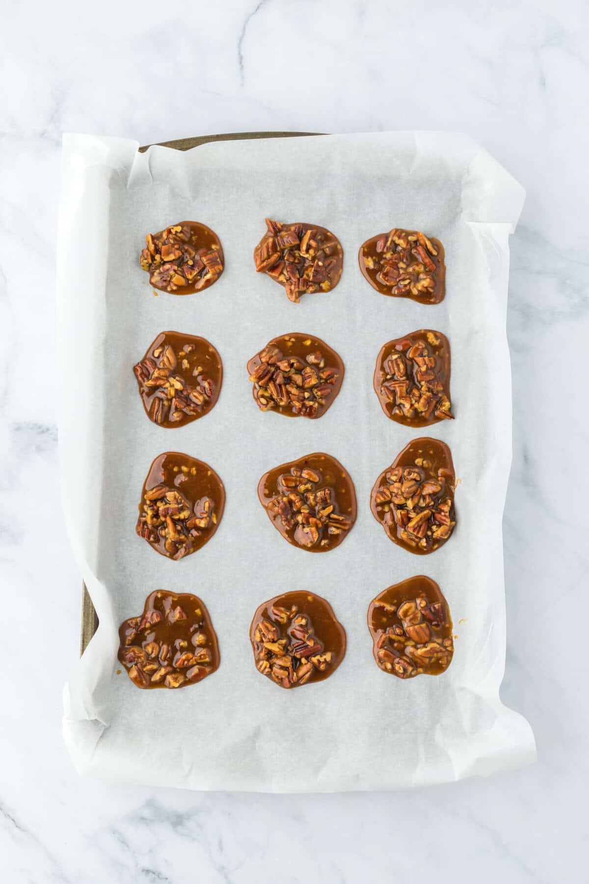 Spooned praline pecans on parchment lined baking sheet waiting to cool and set up