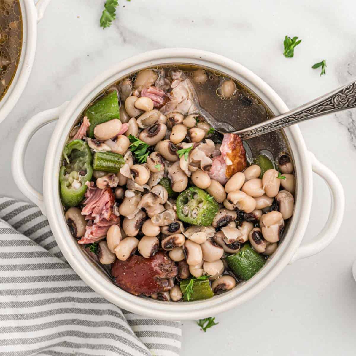 Black Eyed Peas with ham hock in white bowl with cornbread surrounding it for New Year's Day