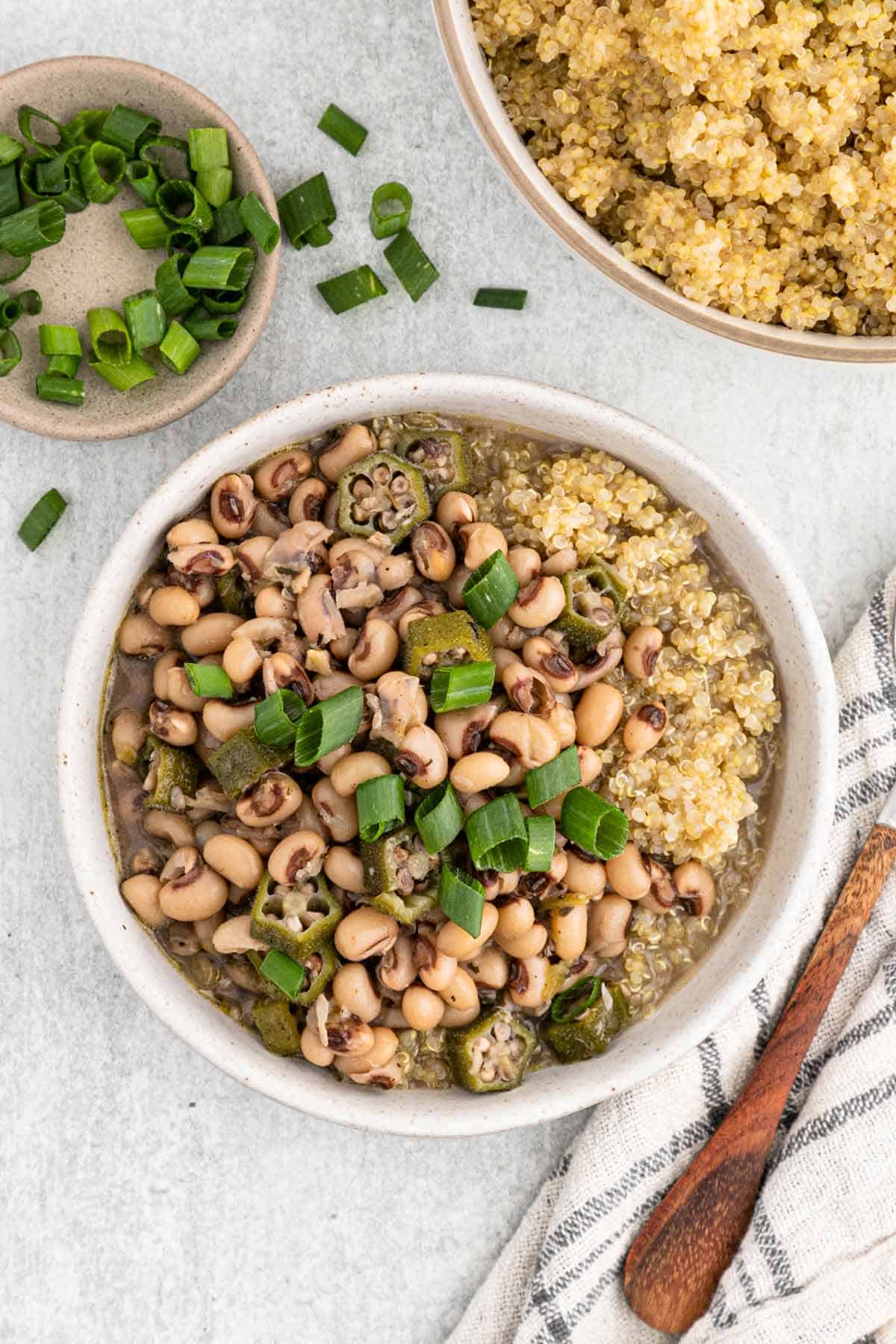 A bowl of hoppin john on the table with quinoa and green onons.
