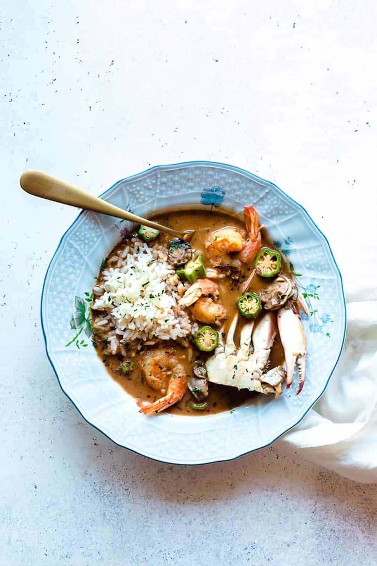 Bowl of seafood gumbo recipe over rice with spoon ready to serve.
