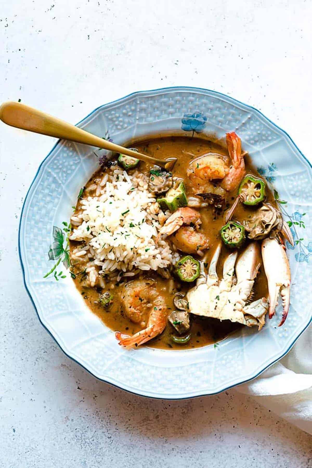 A bowl of seafood gumbo on the table with a spoon in the bowl.