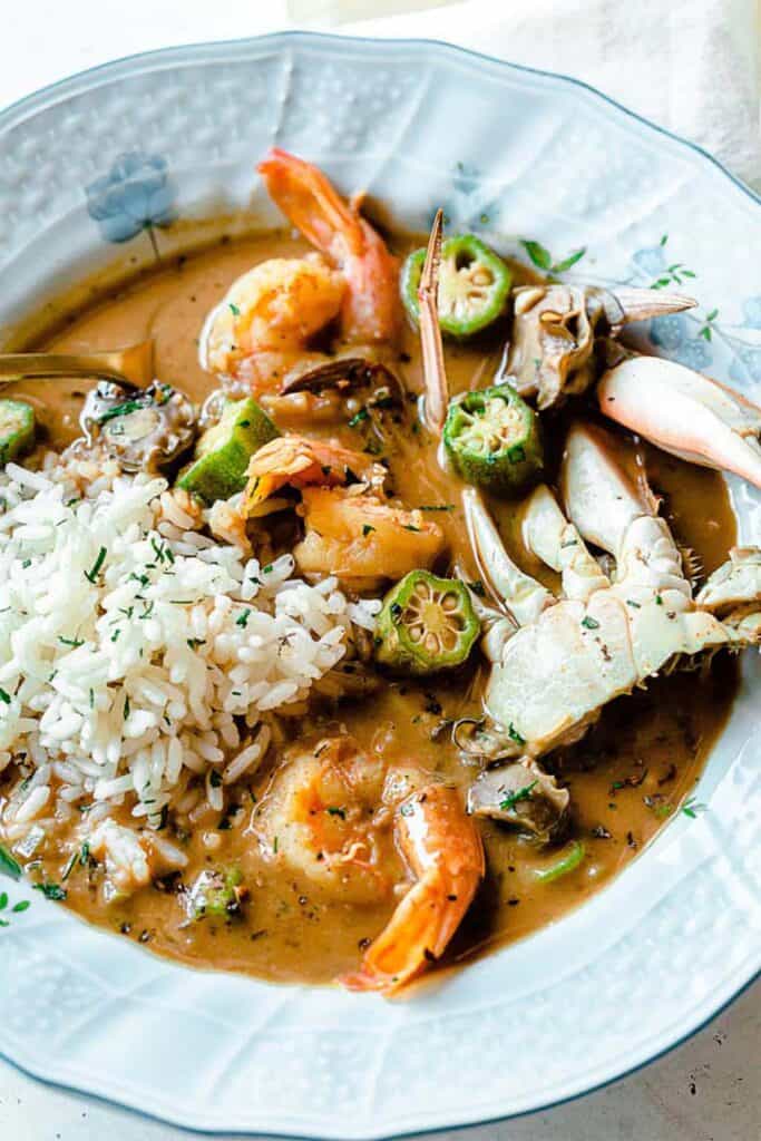 Close up of seafood gumbo in blue bowl with shrimp, crab and okra over rice