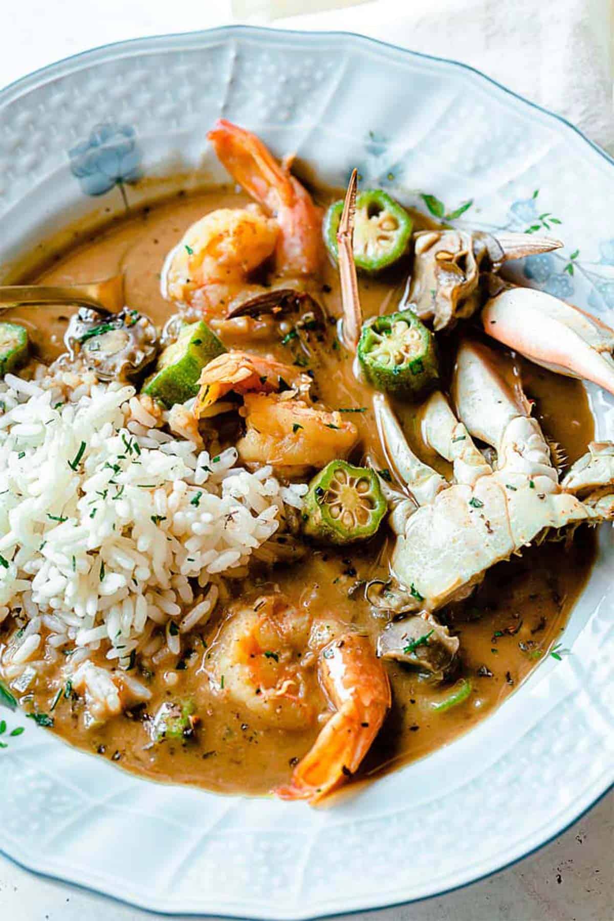 Close up of seafood gumbo in blue bowl with shrimp, crab and okra over rice.