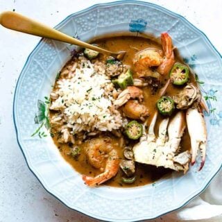 A close up of seafood gumbo recipe in a blue bowl over rice ready to serve for dinner.